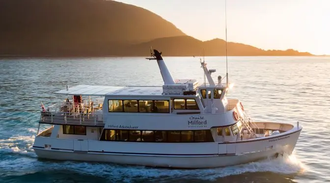 Cruise Milford - large tour boat on the water in Milford Sound during sunset.