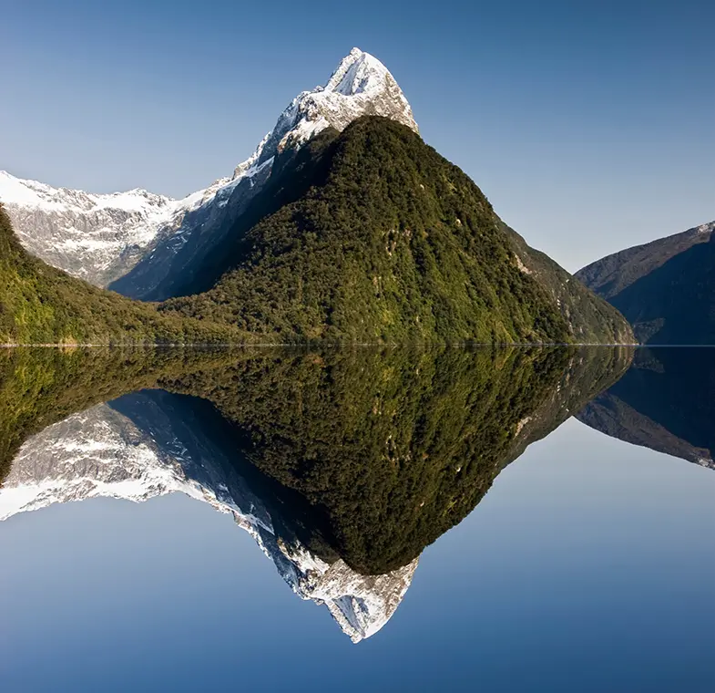 Mitre Peak and its reflection in the calm water, with snow on the peak during winter.